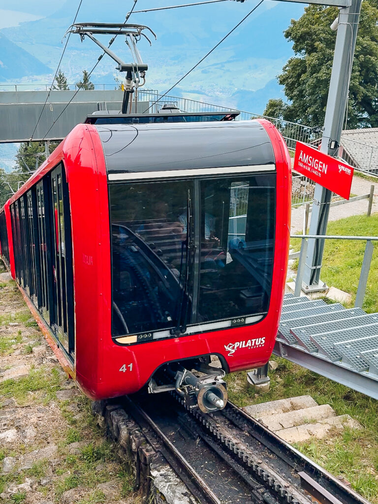 The bright red Pilatus cogwheel train climbing the steep track with mountains and valleys in the distance, transporting you from Lucerne to Mount Pilatus